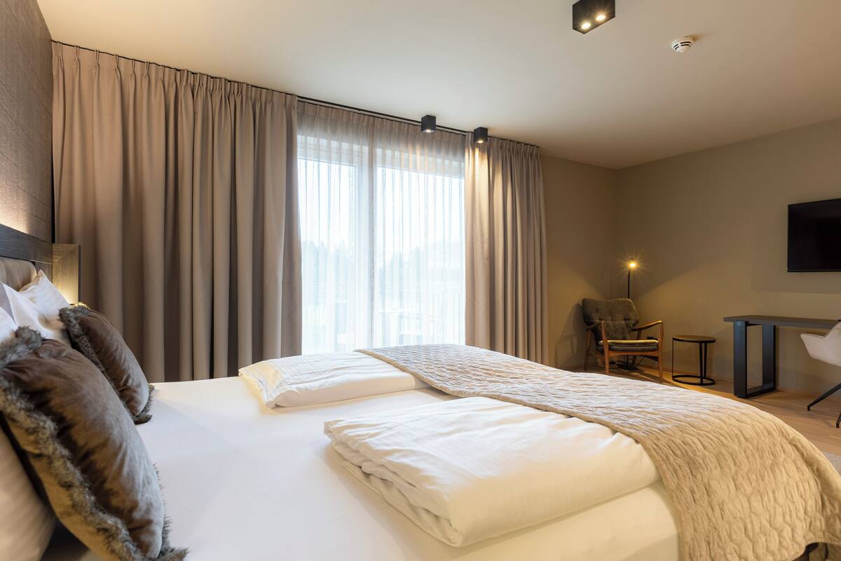Une chambre d’hôtel avec un grand lit, une chaise, un bureau et un téléviseur fixé au mur.