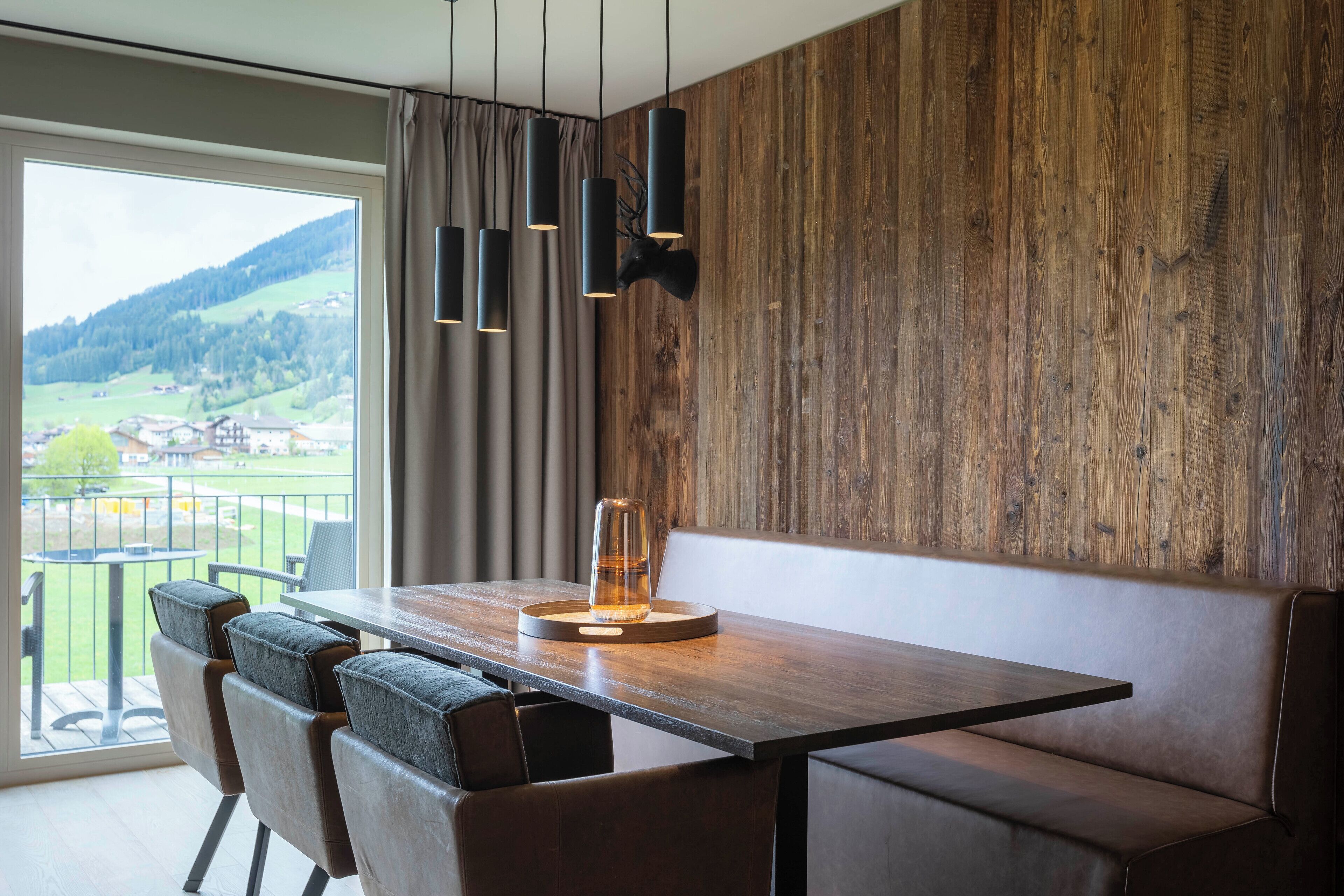 A modern dining area with a wooden wall, a view of a green landscape, and a table with chairs.