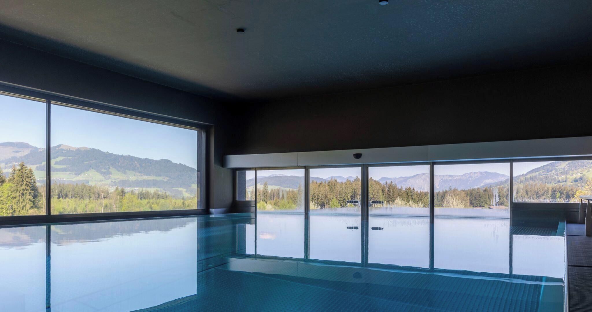 Une grande piscine intérieure offrant une vue sur les montagnes et les arbres.
