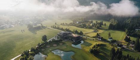 An aerial view of a golf course with a clubhouse, ponds, and surrounding greenery.