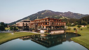 Un bâtiment moderne dont l’image se reflète dans un étang, entouré d’une pelouse bien entretenue et avec une montagne en arrière-plan.