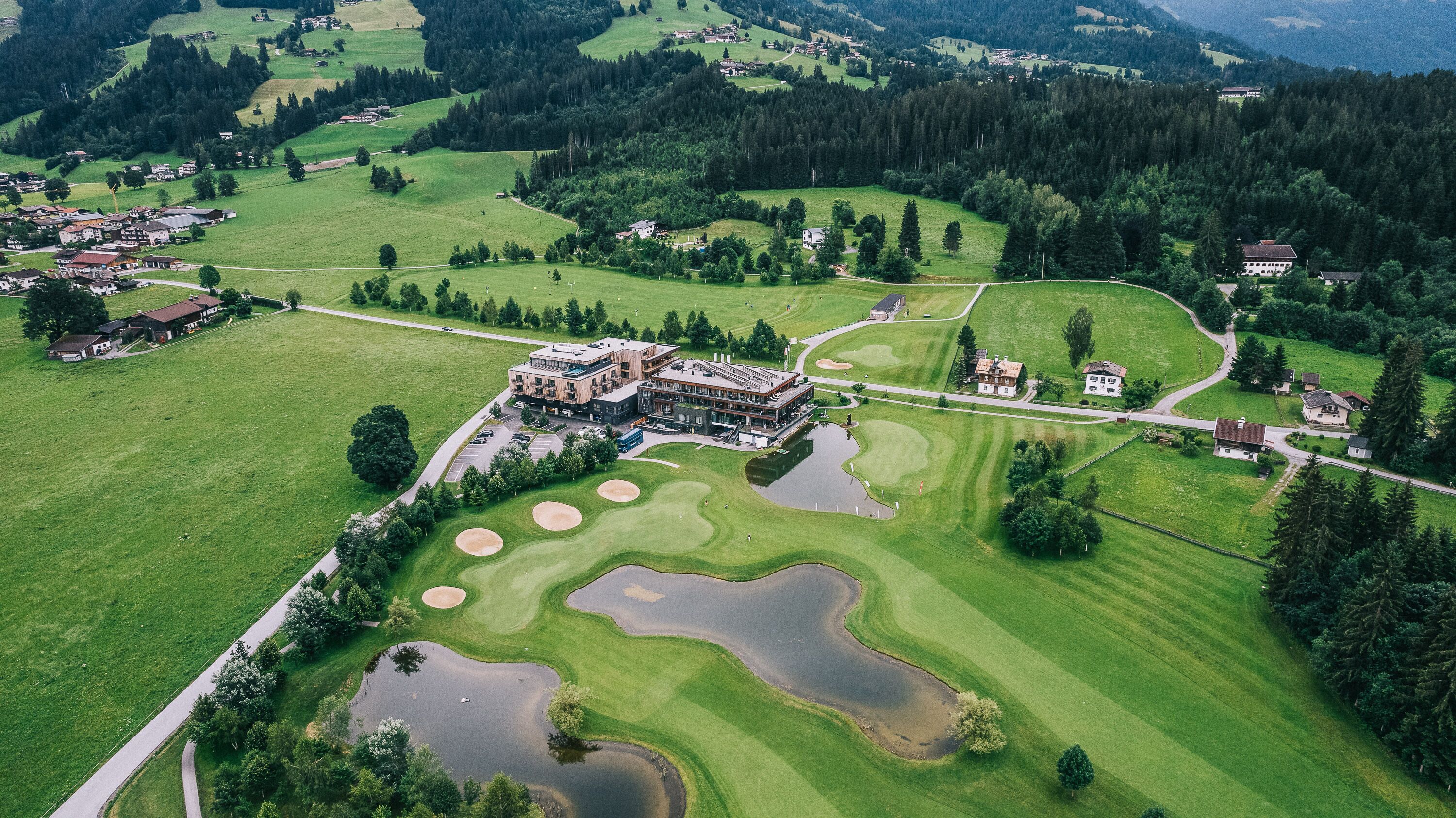 Vista aérea de un campo de golf con un club de campo, varias edificaciones y vegetación circundante.