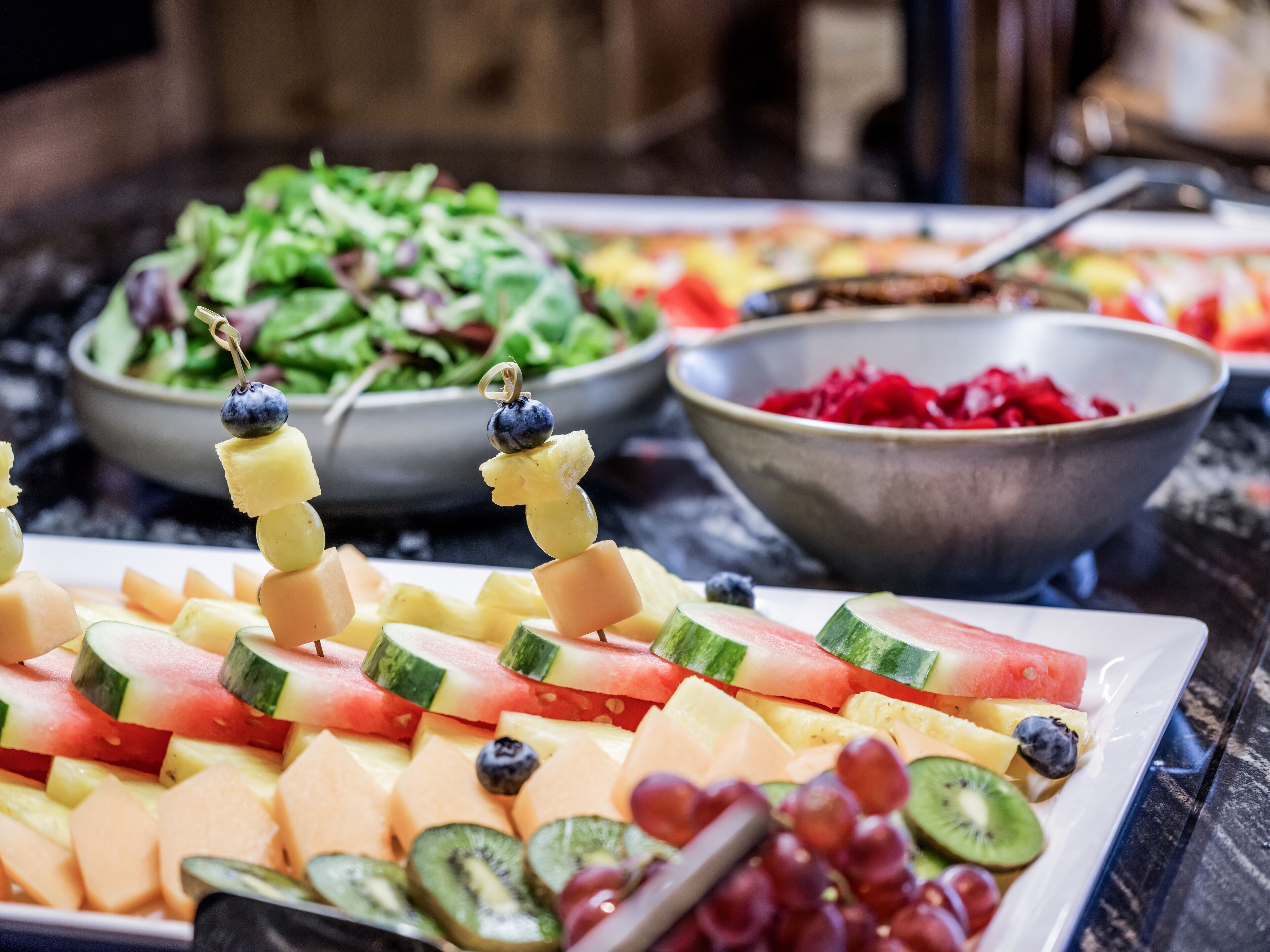 Un buffet proposant une variété de fruits et de légumes, notamment de la pastèque, des kiwis, des raisins et des melons.
