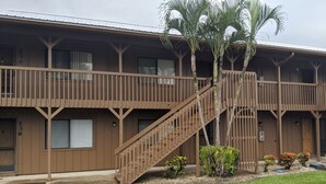 Un motel de dos pisos con una escalera central, habitaciones numeradas y un pequeño jardín.