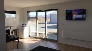A bedroom with a bed, a desk with a chair, a television, and a sliding glass door leading to an outdoor area with a mountain view. - Walking distance to lake Ruataniwha (Twizel)