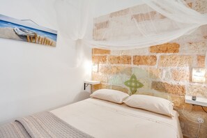 Una camera da letto con una parete a parete in mattoni, un letto con biancheria bianca, un comodino e un quadro raffigurante una barca.