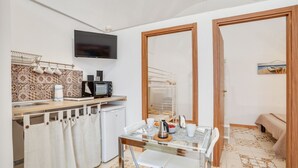 A compact kitchen with a microwave, coffee maker, and a small refrigerator. There is a dining table with chairs and a TV mounted on the wall. - GuestHost - Bright apartment equipped with every comfort to accommodate up to 4 people and located in the center of Polignano, in an area equipped with all essential services, easily reachable on foot. The flat is 400 meters from the lively Piazza Vittor (Polignano a Mare)