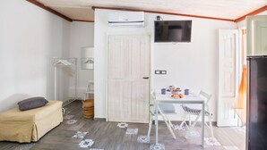 Una habitación pequeña con cama, una mesa y sillas, televisión y aire acondicionado.