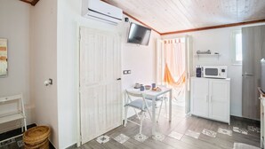 Una habitación pequeña y acogedora con techo de madera, una puerta blanca, una mesa con sillas, un televisor y un microondas.