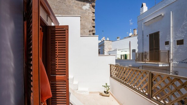 Un callejón estrecho con una cerca de madera, una planta en maceta y un edificio de fachada blanca con un balcón.