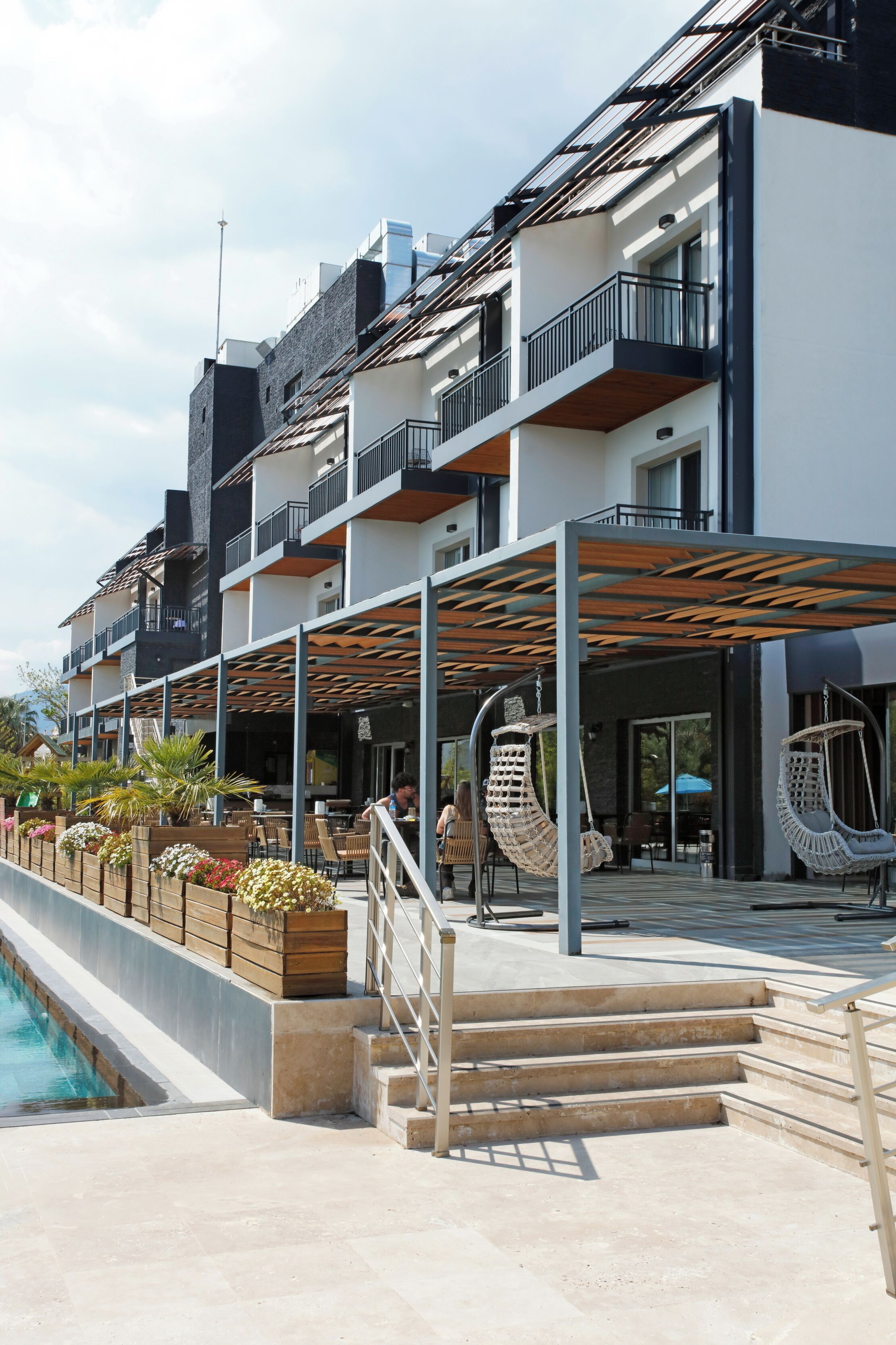 A modern hotel with outdoor seating, a pool, and a covered patio area.