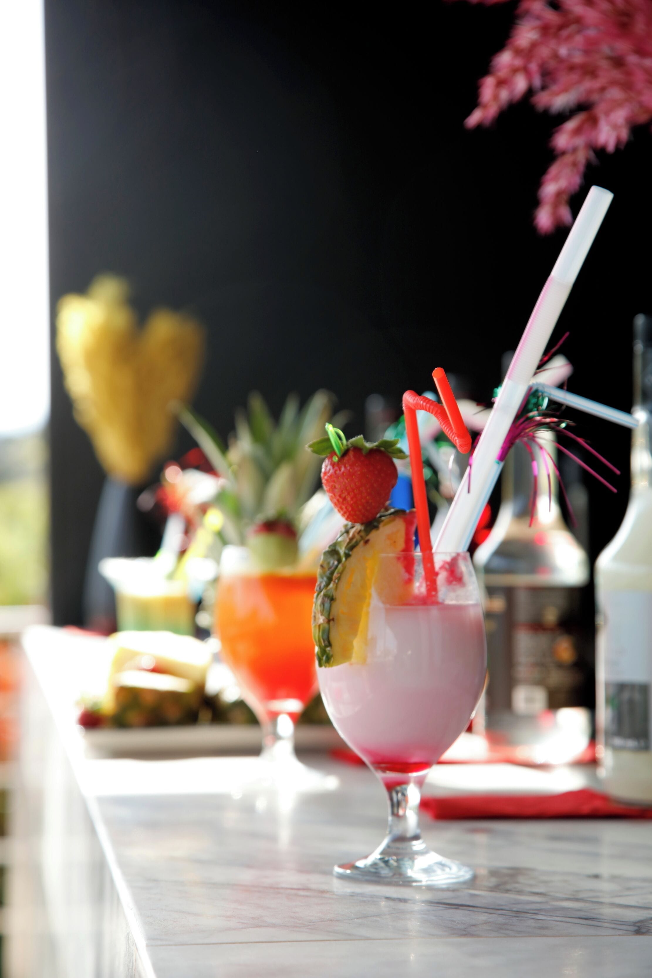 Eine Bar mit einem Getränk, verziert mit Erdbeere und Ananas, und mehreren Trinkhalmen.