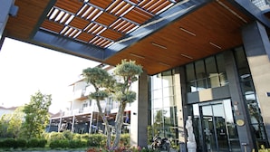 A modern building with a wooden slatted roof, a paved entrance area, and a statue in front. - Allia Thermal Health & Spa Kazdagları (Edremit)