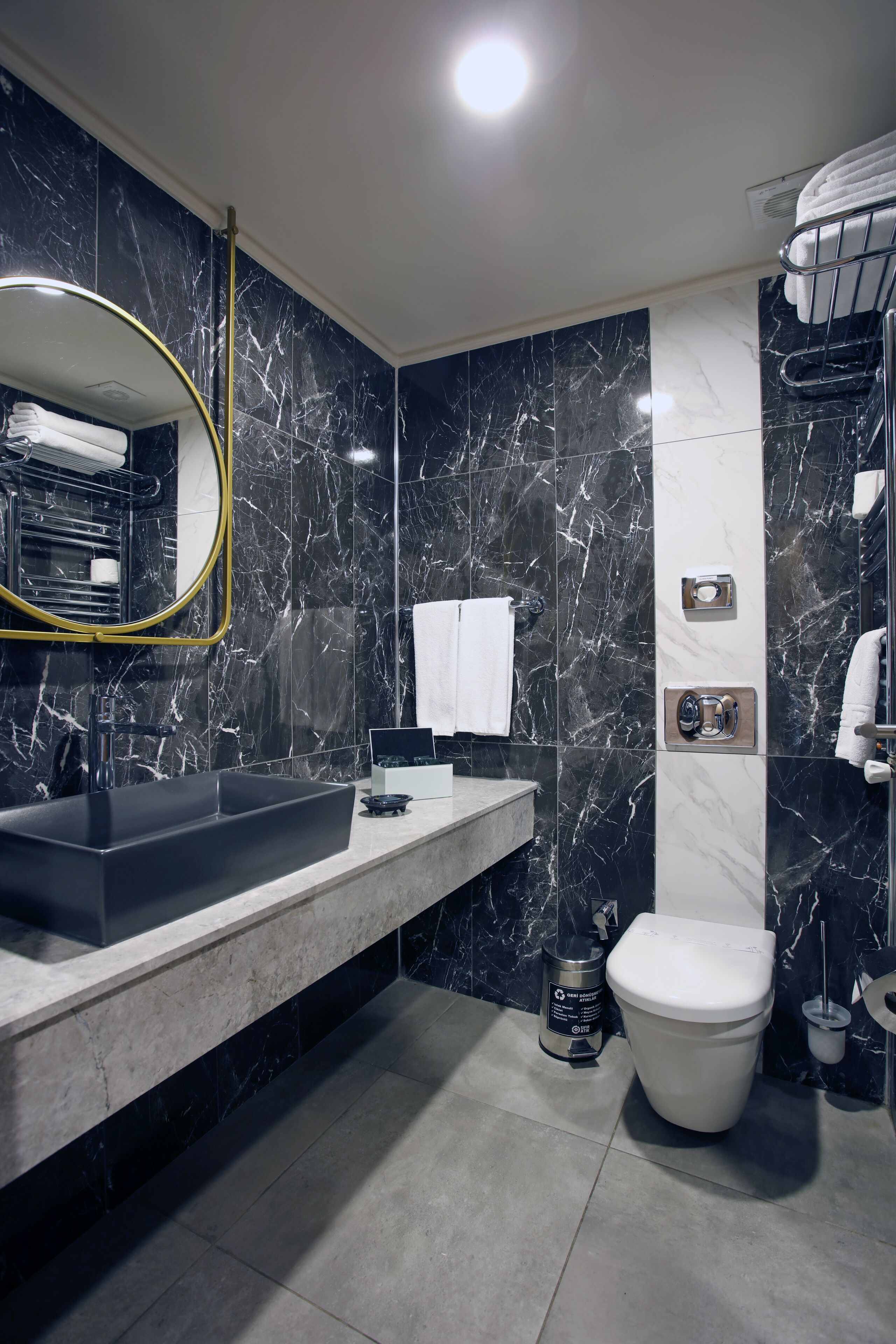 A modern bathroom with a black marble wall, a large mirror, a sink, a toilet, and a shower area.