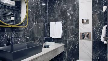Un baño moderno con pared de mármol negro, un espejo grande, un lavamanos, un inodoro y una zona de ducha.