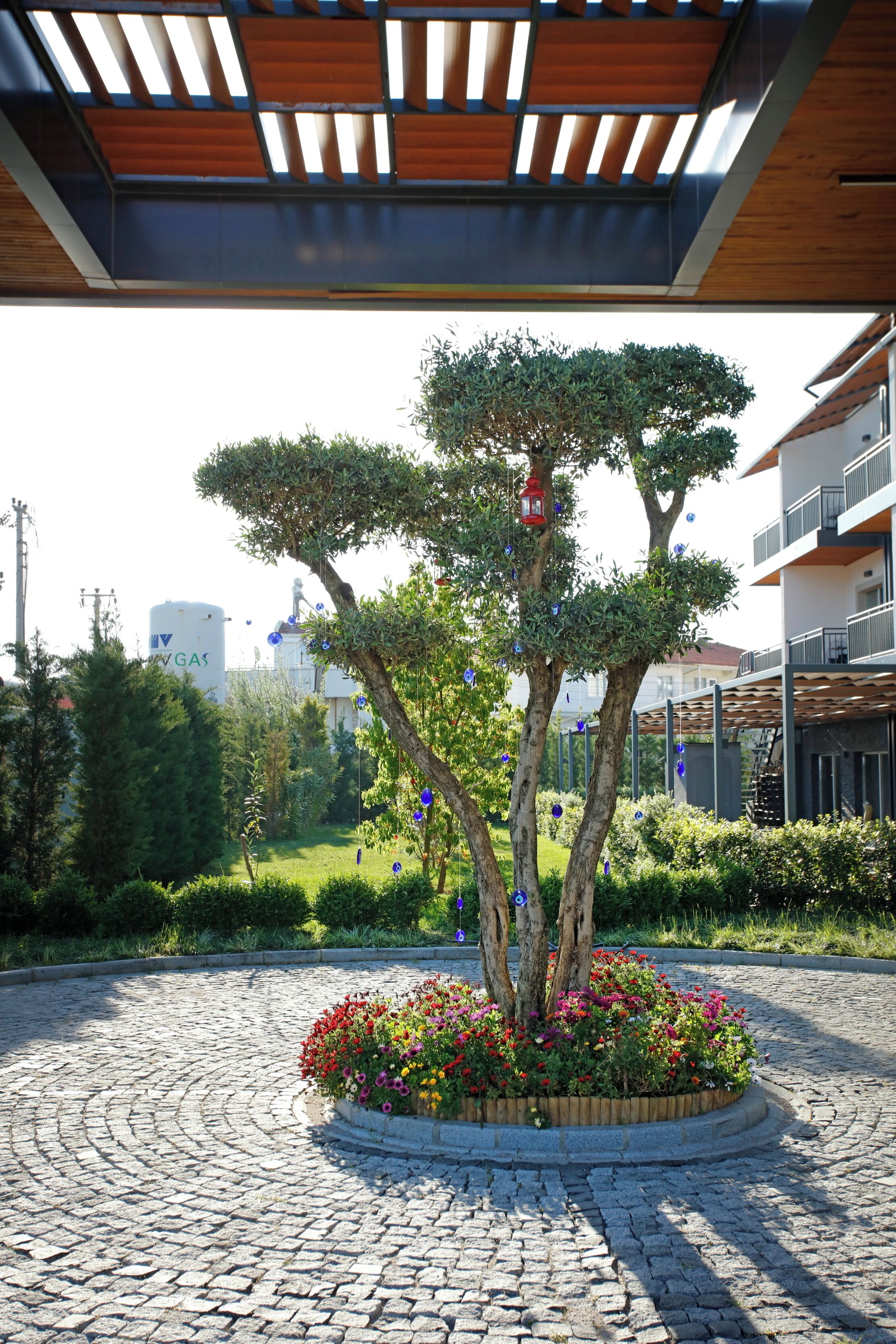 A cobblestone courtyard with a central tree and flower bed, surrounded by buildings.