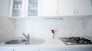 Una cocina con armarios blancos, un lavamanos de acero inoxidable y una estufa a gas.