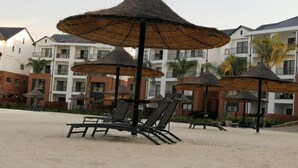 A beachside resort with thatched umbrellas, lounge chairs, and multi-story buildings in the background. - The Blyde 1317 (Pretoria)
