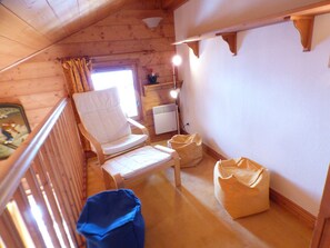 A cozy attic bedroom with a wooden sloped ceiling, a white chair, a small table, and a radiator.