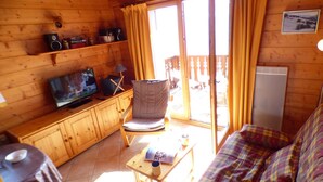 Interior acogedor de una cabaña con piso de madera, un sofá, un televisor, una mesita y una silla.