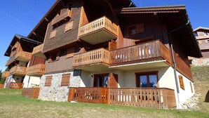 Una cabaña de madera de varios pisos con balcones, muros de piedra y un jardín delantero cubierto de césped.