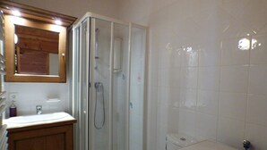 Un baño con ducha de vidrio, tocador de madera y lavamanos blanco.