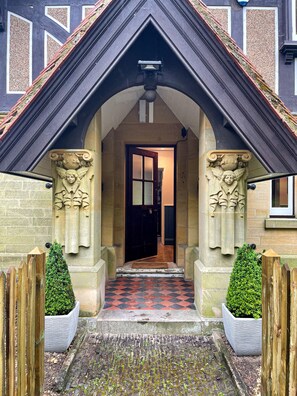 A building entrance with a black roof, a tiled pathway, and two stone statues on either side.
