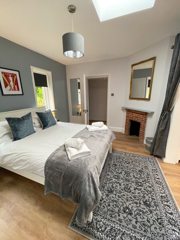 A bedroom with a bed, bedside tables, a mirror, a fireplace, and a window.