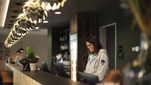 A reception desk with a modern design, including a unique hanging light fixture and a potted plant. - Holiday Inn - the niu, Hop Forchheim by IHG (Forchheim)