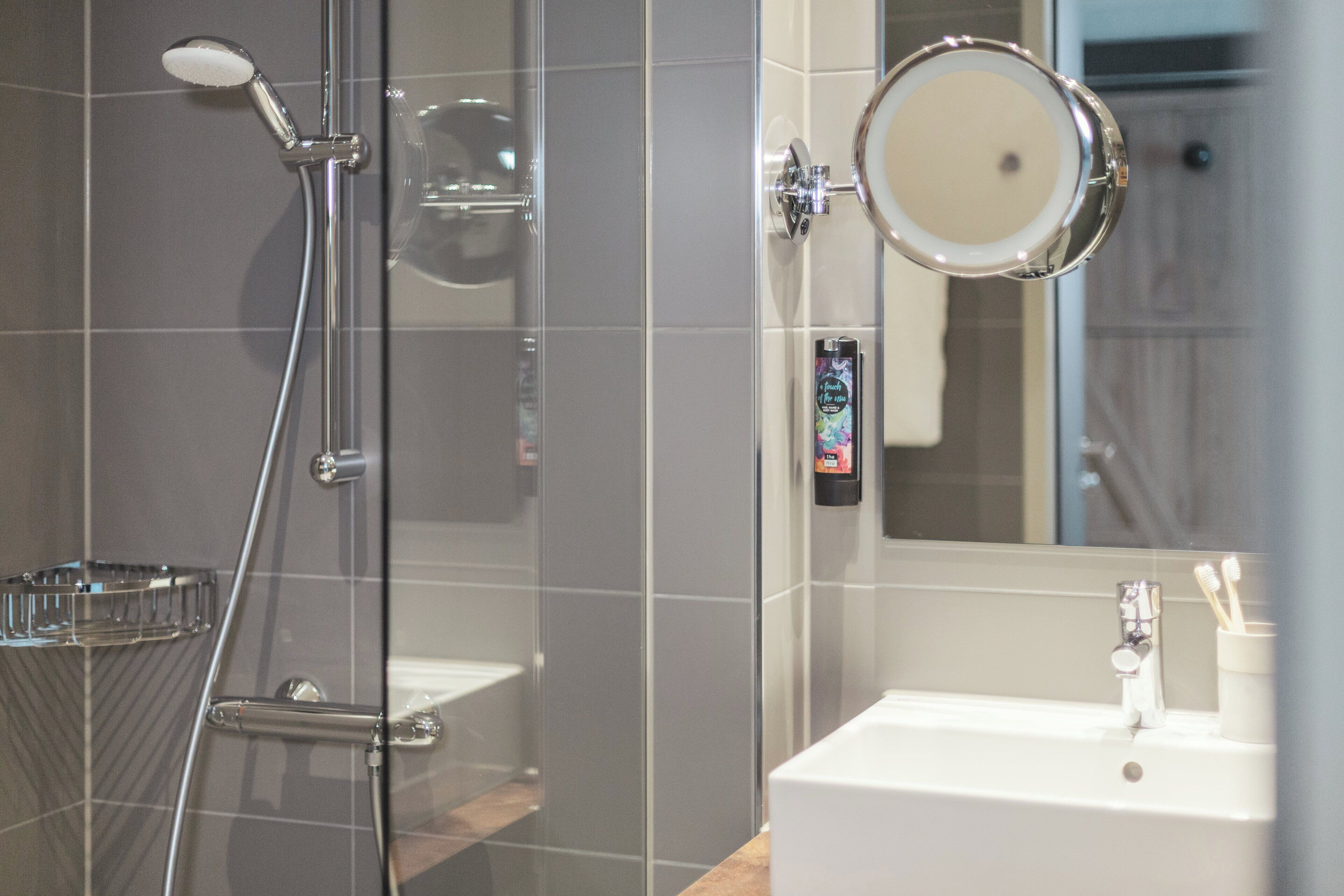 Un baño moderno con cabina de ducha de vidrio, un lavabo blanco y un cabezal de ducha manual.