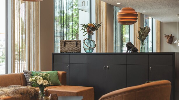 A modern living room with a sofa, ottoman, and a small table with a vase of flowers. - Holiday Inn - the niu, Hop Forchheim by IHG (Forchheim)