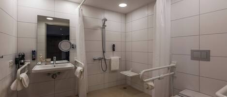 Ein modernes Badezimmer mit Waschbecken, Spiegel, Toilette, Dusche und Haltegriffen.