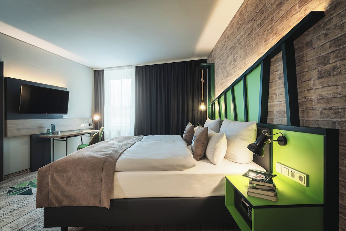 A modern hotel room with a large bed, a desk, a flat-screen TV, and a green accent wall.