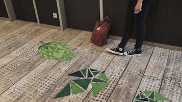 En person står i en hall med ett mönstrat golv, en brun väska och ett grönt, geometriskt föremål på golvet.