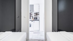 Et moderne hotelværelse med to senge, et synligt tekøkken med vaskemaskine, og et badeværelse med toilet og håndvask.