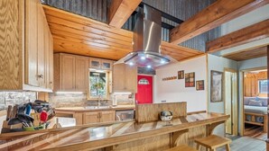 Una cocina moderna con armarios de madera, una isla central con taburetes, un refrigerador rojo y un ventanal grande.