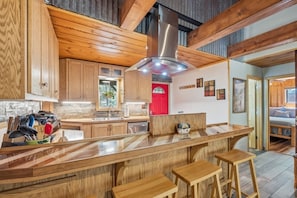 Cozinha moderna com armários de madeira, uma ilha central com bancos, geladeira vermelha e uma janela grande.