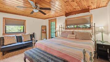 Un dormitorio con techo de madera, una cama con colcha a rayas, un banco, una mesita de noche y una ventana con persianas.