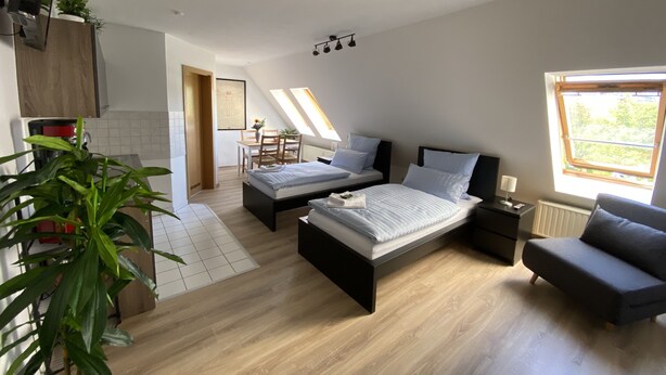A modern loft bedroom with a large bed, a sofa, a dining area, and a kitchen. - Ferienwohnung am Jacobsweg (Wurzen)