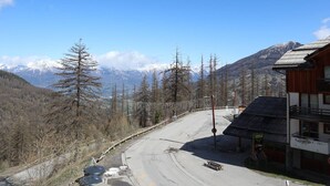 A mountain road with a wooden building on the right, surrounded by trees and snow-capped mountains in the background. - Cozy apartment with pool, sleeps 4, Les Orres 1800 (Les Orres)