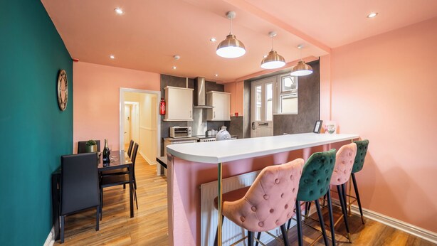 Een moderne keuken met een centraal eiland, barstoelen en een eethoek met stoelen.