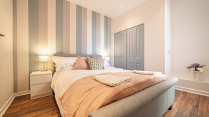 Een keurig opgemaakt slaapkamer met een bed, nachtkastjes, een kledingkast en een muur met verticale strepen.