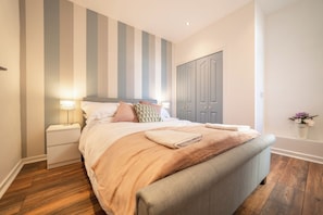 A neatly arranged bedroom with a bed, nightstands, a wardrobe, and a wall with vertical stripes.
