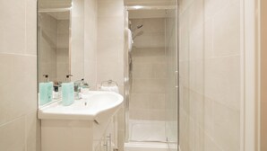 Een moderne badkamer met een douchecabine van glas, een witte wastafel met toiletartikelen en een spiegel.