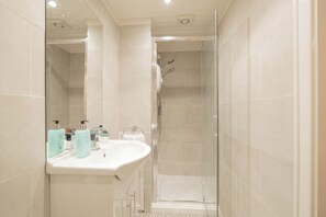 Une salle de bain moderne avec une douche à parois de verre, un lavabo blanc agrémenté d’articles de toilette et un miroir.
