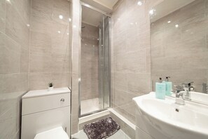 Un baño moderno con cabina de ducha de vidrio, un lavabo blanco con espejo y una pequeña planta en maceta sobre el mueble.