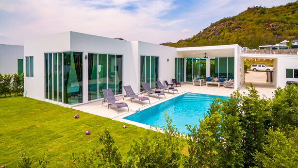 Uma casa moderna com piscina, amplas janelas de vidro e um gramado bem cuidado.