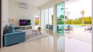 Uma sala de estar moderna com televisão de tela plana, um sofá azul, uma mesa de centro pequena e uma porta de vidro que dá para uma área de piscina externa.