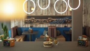 A cozy restaurant interior with a wooden wall, cushioned seating, and hanging circular light fixtures. - Holiday Inn - the niu, Brass Munich Olympiapark by IHG (Munich)