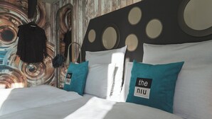 A neatly made bed with white linens and teal pillows, a wooden headboard with circular designs, and a wall with a swirling abstract pattern. - Holiday Inn - the niu, Brass Munich Olympiapark by IHG (Munich)